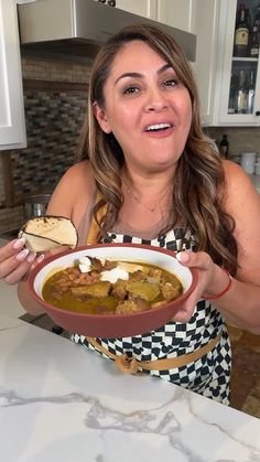 a woman is holding a bowl of soup in her hands and looking at the camera