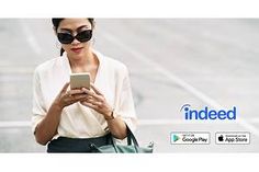 a woman in sunglasses looking at her cell phone while walking down the street with an advertisement for indeedd