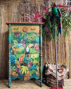 a colorful painted dresser next to a bird cage and potted plant in front of it