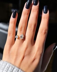 a woman's hand with a black manicure and a diamond ring on it