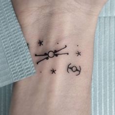 a small wrist tattoo with the symbols for zodiacs and stars in black ink on it