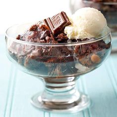 a glass bowl filled with ice cream and chocolate brownie desert on top of a blue table