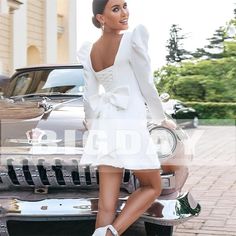 a woman standing on the hood of a car in front of a building and posing for a photo