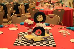 a red table topped with a yellow car next to a vase filled with white and red flowers