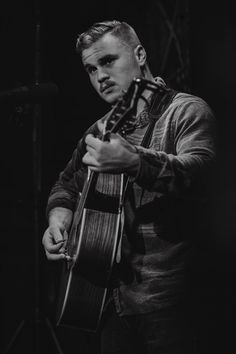 a man holding a guitar while standing in front of a microphone