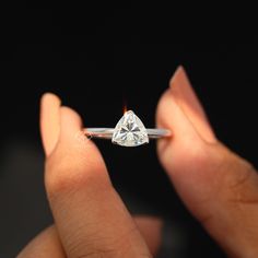 a woman's hand holding a diamond ring in front of her face with the light shining through it