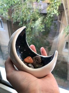 a hand holding a black and white bowl with rocks in it on a window sill