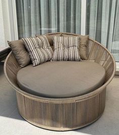 a round wicker couch sitting on top of a cement floor next to a window