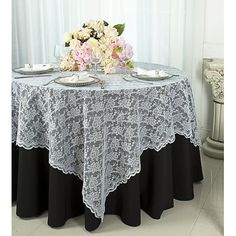 the table is set with two plates and flowers in front of it on top of a black table cloth