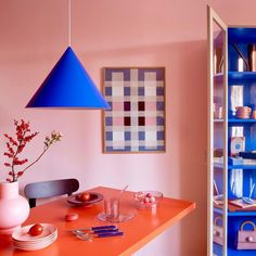 an orange table topped with plates and vases next to a blue shelf filled with dishes