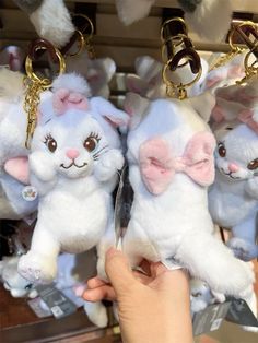 several white stuffed animals with pink bows on their ears are being held by someone's hand