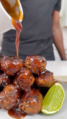 a person pouring sauce over some food on a plate with limes and a slice of lime