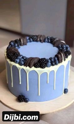 a blue cake with white icing and blackberries on the top is sitting on a plate