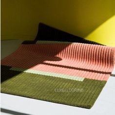 an area rug on the floor in front of a yellow wall with sunlight coming through it