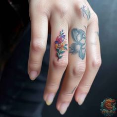 a woman's hand with tattoos and flowers on her fingers, holding onto the ring