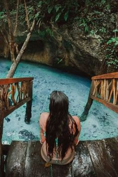 a woman sitting on a wooden bridge looking down at the blue water in a pool