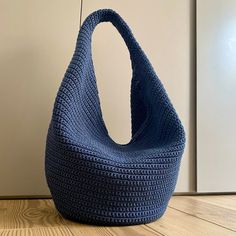 a blue crocheted bag sitting on top of a wooden floor next to a white wall