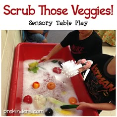 a young boy is playing with some sort of food in a red tray that says scrub those veggies