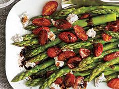 asparagus with tomatoes and goat cheese on a white plate next to silverware