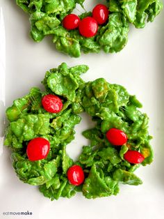 christmas wreath shaped cookies with cherries on them sitting on a white plate, ready to be eaten