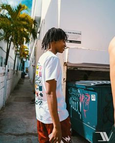 a man with dreadlocks standing next to a trash can