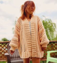 a woman standing in front of a wooden bench wearing a crocheted cardigan