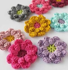 small crocheted flowers are arranged on a white surface, each with different colors