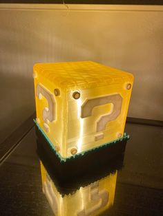 a yellow plastic object sitting on top of a black table next to a mirror with question marks