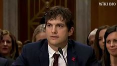 a man in a suit and tie sitting at a table with other people behind him