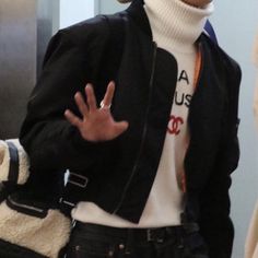 a man in black jacket and white shirt holding his hand out to the side while standing next to an elevator