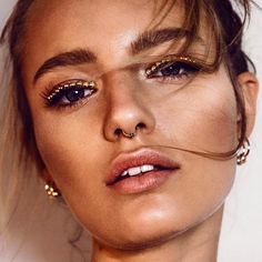 a close up of a person wearing gold eyeliners and piercings on her nose