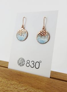 a pair of earrings sitting on top of a wooden table next to a white card