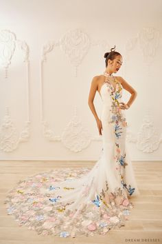 a woman standing in front of a white wall wearing a dress with flowers on it