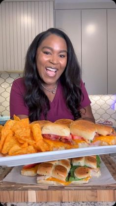 a woman sitting in front of two trays filled with sandwiches and chips