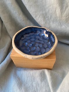 a blue bowl sitting on top of a wooden stand in front of a gray cloth