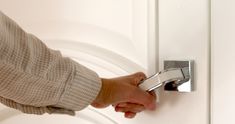 a person's hand is holding onto the handle of a door knob on a white door