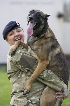 a woman in uniform holding a large brown and black dog with its tongue hanging out