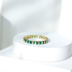 a gold ring with emeralds on it sitting on top of a white stand in front of a white wall