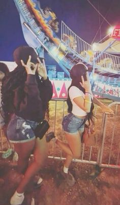 two young women standing next to each other in front of a roller coaster