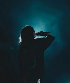 a person standing in the dark with their hands up to their face while holding something