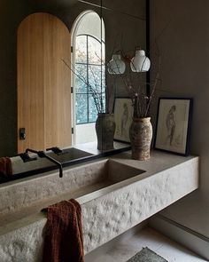 a bathroom sink sitting under a window next to a mirror and vase with flowers in it