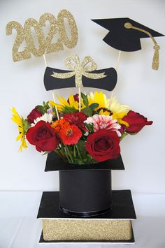 a bouquet of flowers in a black vase with gold glitter graduation decorations on the top