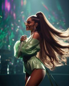 a woman with long hair and glasses on stage holding a microphone in her hand while wearing a green dress