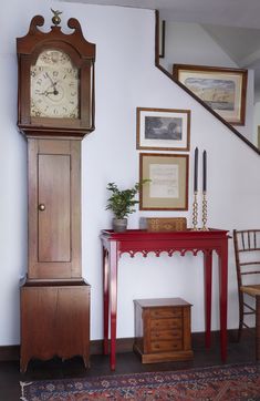 a grandfather clock sitting on top of a wooden table next to a red desk and chair