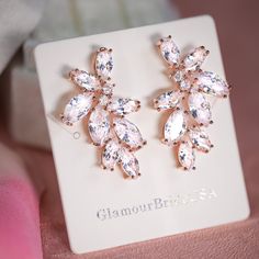 a pair of pink crystal earrings sitting on top of a white box next to a stuffed animal