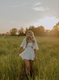 a woman in a white dress walking through tall grass