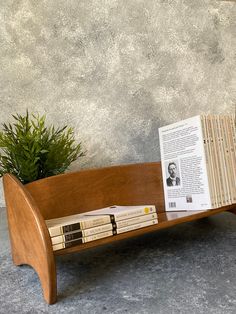 a wooden book stand holding books and a potted plant on the table next to it