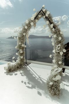 an arch decorated with white flowers on top of a roof next to the ocean and sky