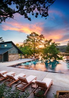 an outdoor swimming pool with lounge chairs next to it and the sun setting in the background