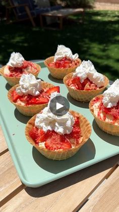 small pies with whipped cream and strawberries on a blue tray in the sun